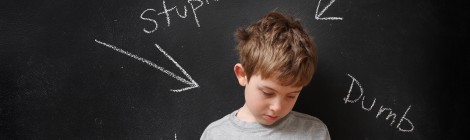 picture of bullied boy standing in front of hurtful words on chalkboard
