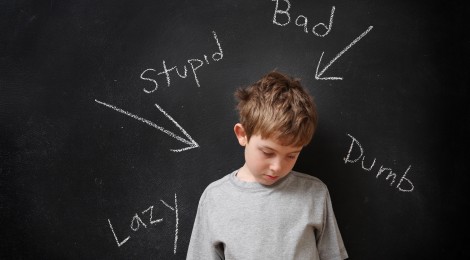 picture of bullied boy standing in front of hurtful words on chalkboard